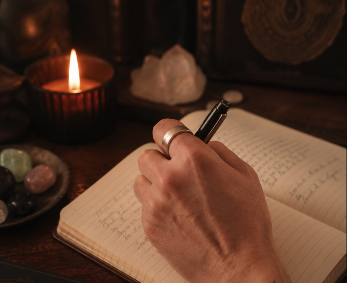 Hand writing in a journal beside candles and crystals — the craft of a written reading